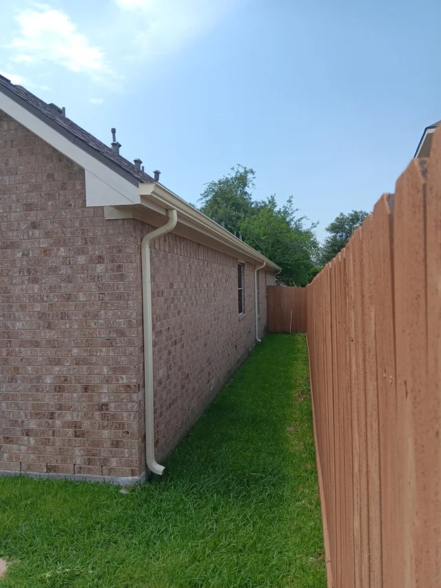 White downspout beside a brick side wall and fenced yard