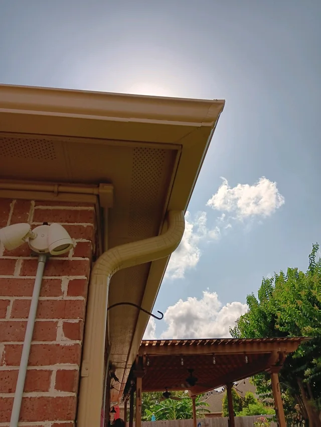 Pale gutter and downspout at the corner of a brick home