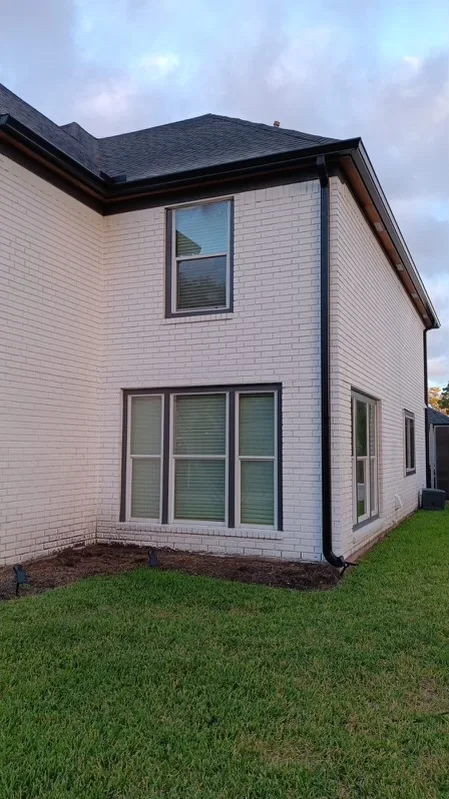 Black downspout contrasting with light siding and brick