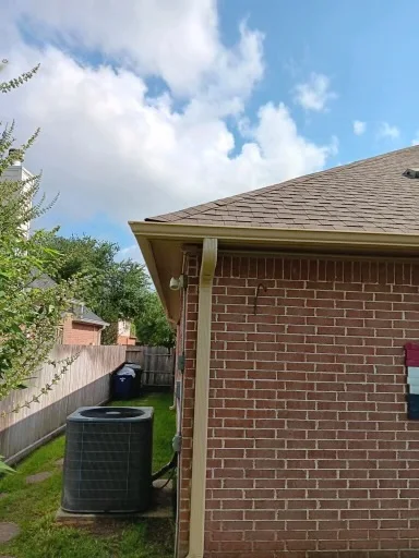 Pale gutter and downspout at the corner of a brick home