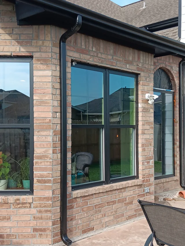 Black downspout contrasting with light siding and brick