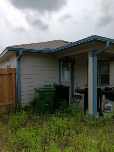 Blue gutter and downspout beside a brick house and fenced yard
