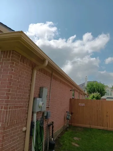 White downspout beside a brick side wall and fenced yard
