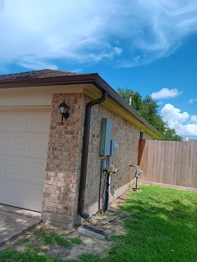 White downspout beside a brick side wall and fenced yard