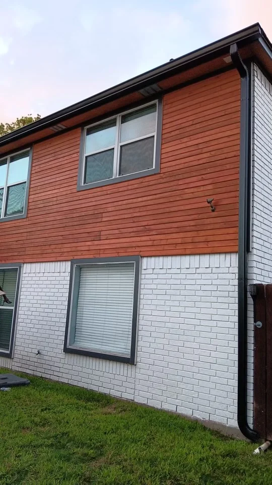 Black downspout contrasting with light siding and brick