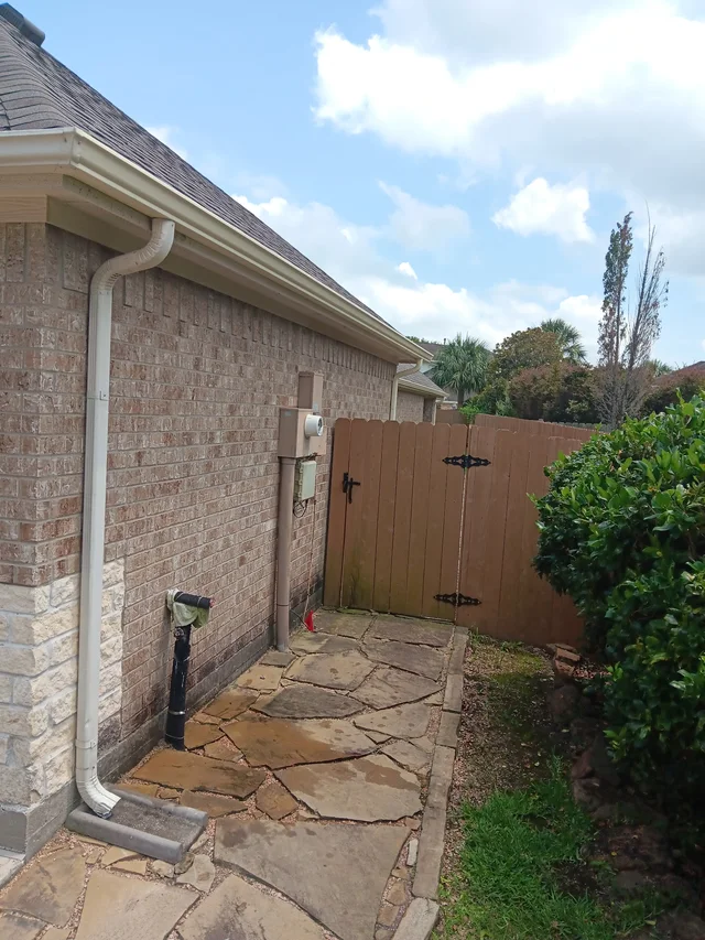White downspout beside a brick side wall and fenced yard