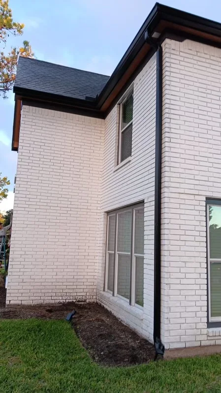 Black downspout contrasting with light siding and brick
