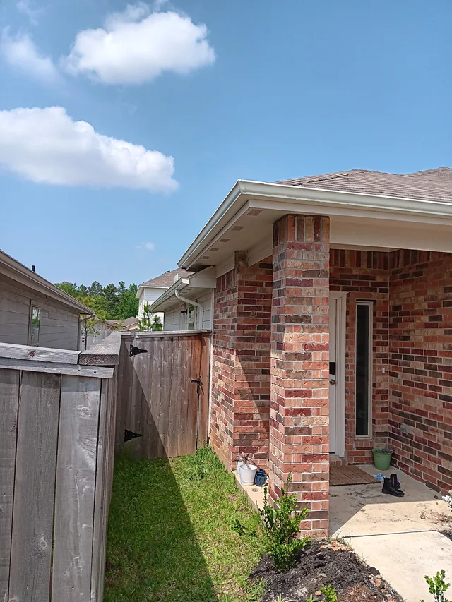 White downspout beside a brick side wall and fenced yard