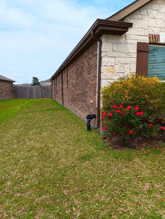 White downspout beside a brick side wall and fenced yard