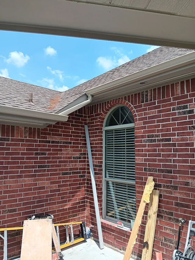 Gutter and downspout above a brick patio with construction materials