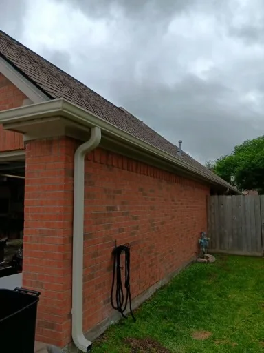 Pale gutter and downspout at the corner of a brick home