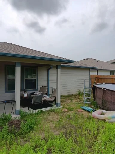Blue gutter and downspout beside a brick house and fenced yard