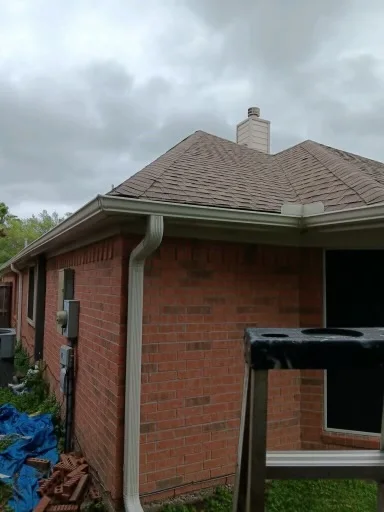 Pale gutter and downspout at the corner of a brick home
