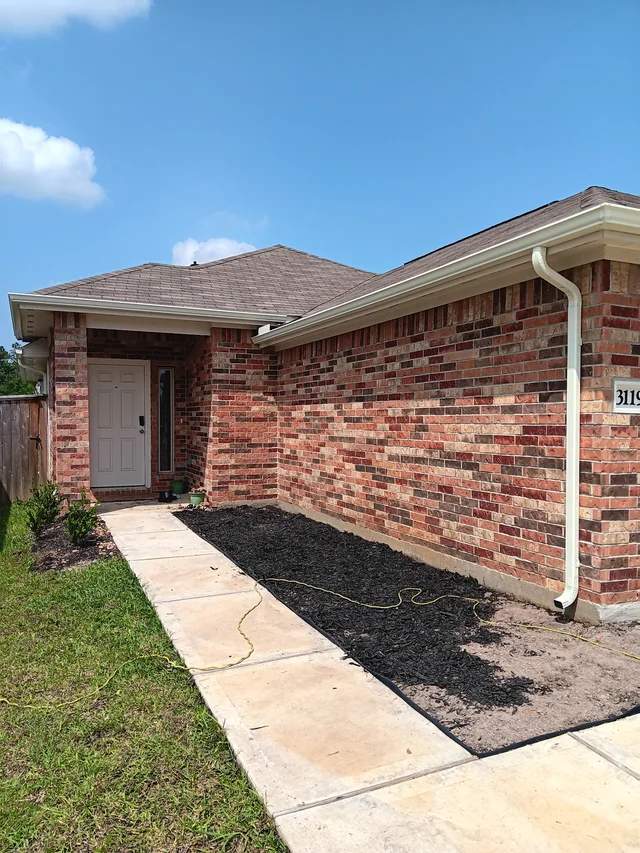 White downspout beside a brick side wall and fenced yard