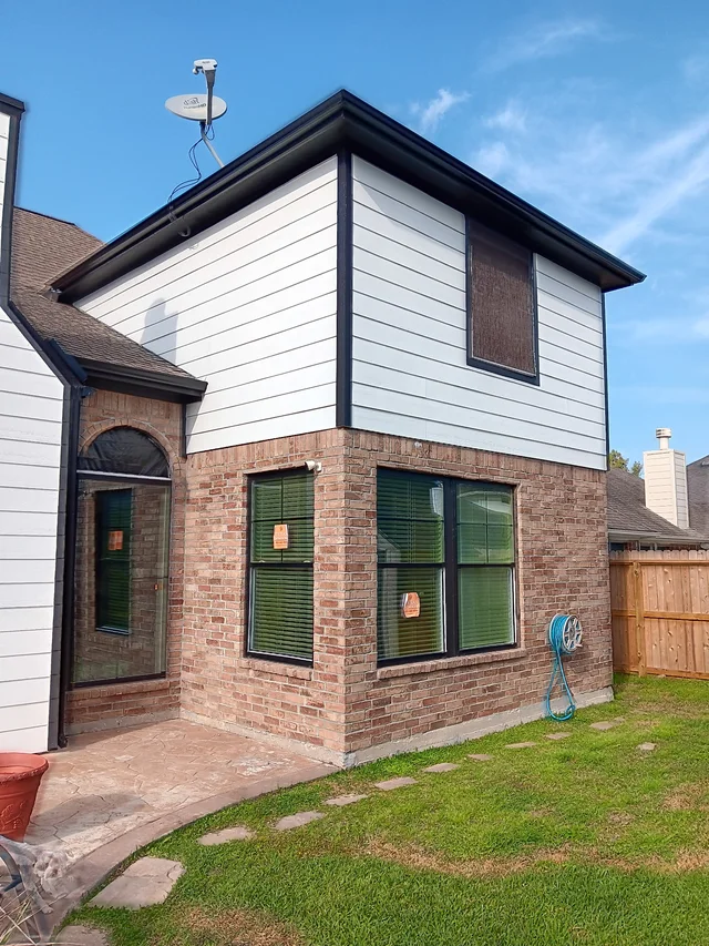 Black downspout contrasting with light siding and brick