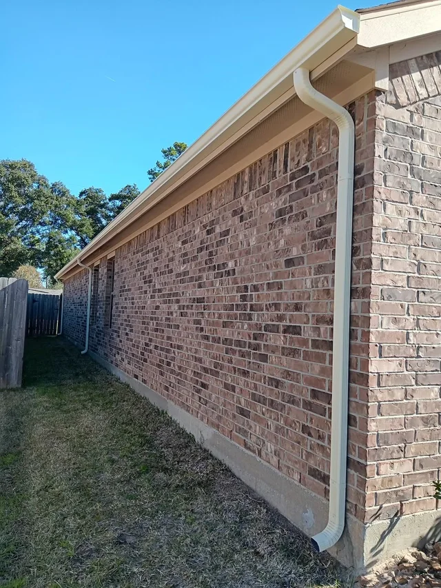 White downspout beside a brick side wall and fenced yard