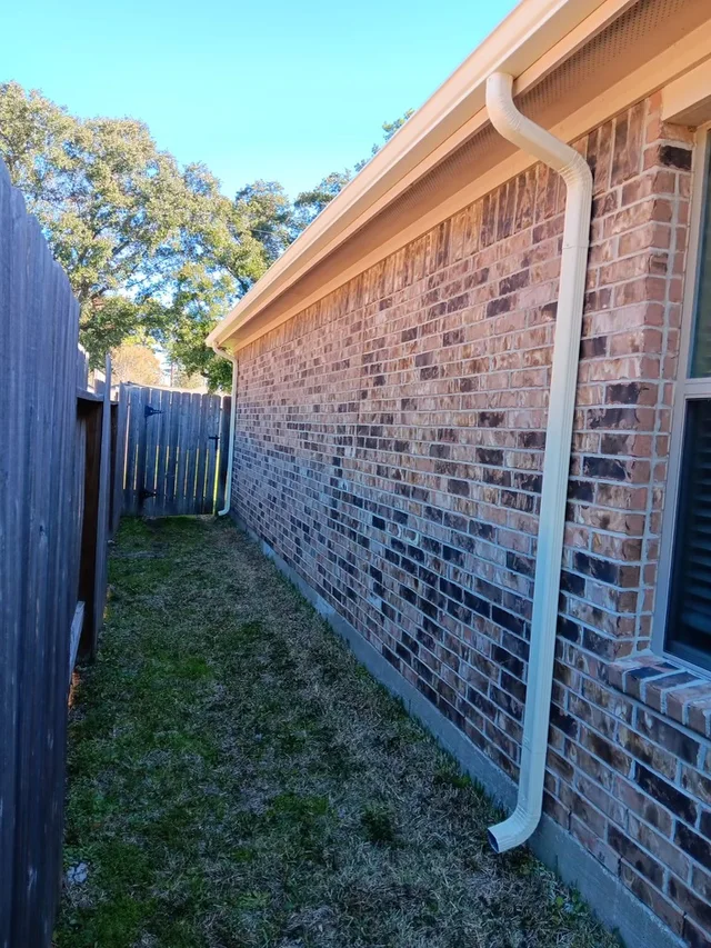 White downspout beside a brick side wall and fenced yard