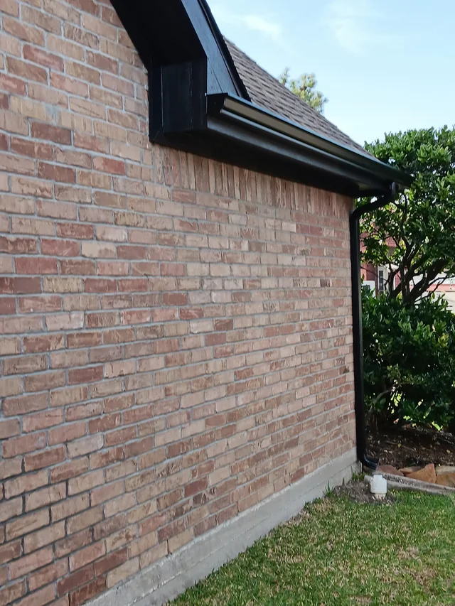 Black downspout contrasting with light siding and brick