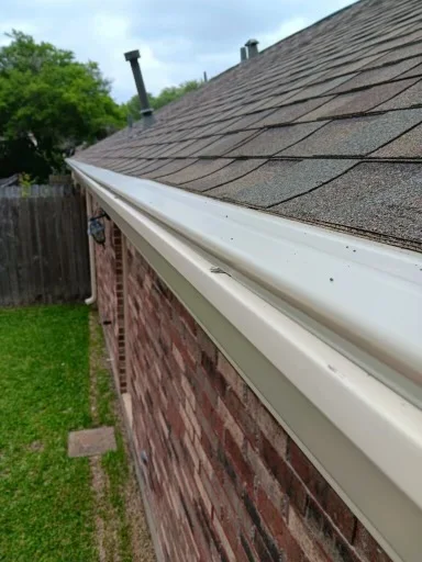 View along the open gutter channel at a shingle roof edge