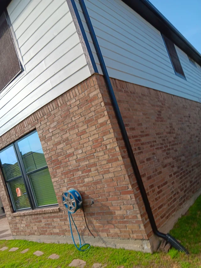 Black downspout contrasting with light siding and brick
