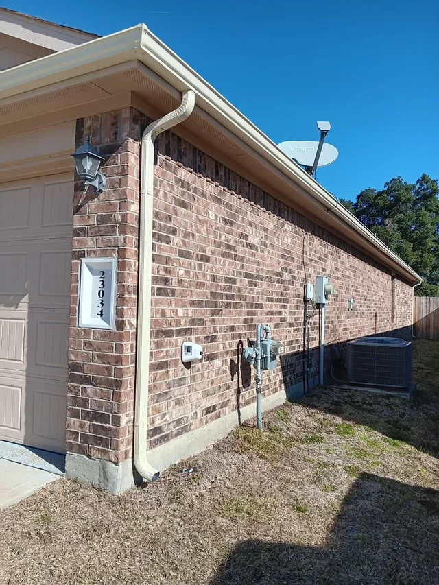 White downspout beside a brick side wall and fenced yard