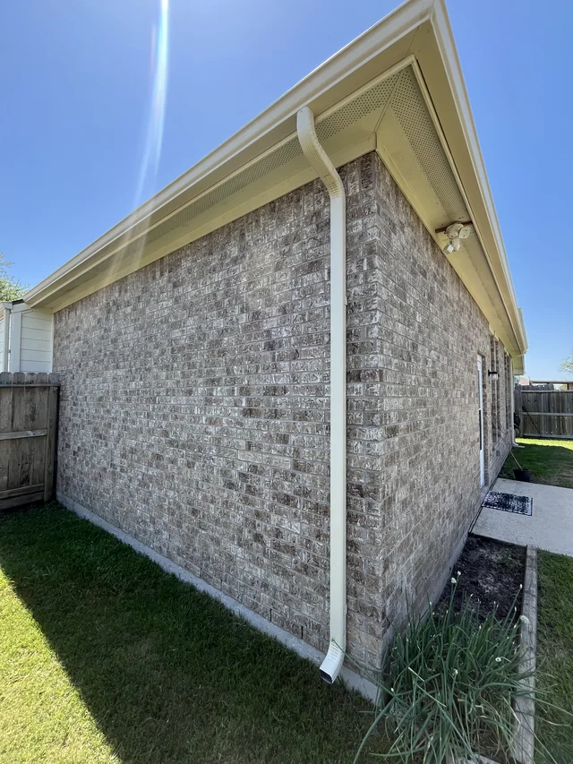 White downspout beside a brick side wall and fenced yard