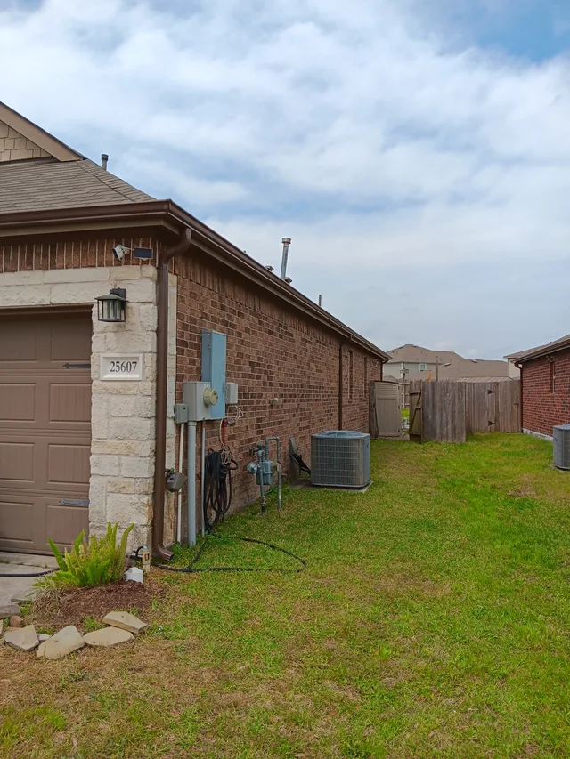 White downspout beside a brick side wall and fenced yard