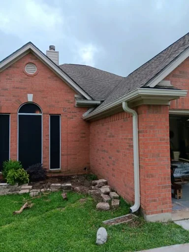 Pale gutter and downspout at the corner of a brick home